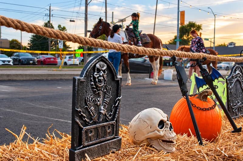 A decorative skull, pumpkin and gravestone sit on straw beside the pony-ride area.