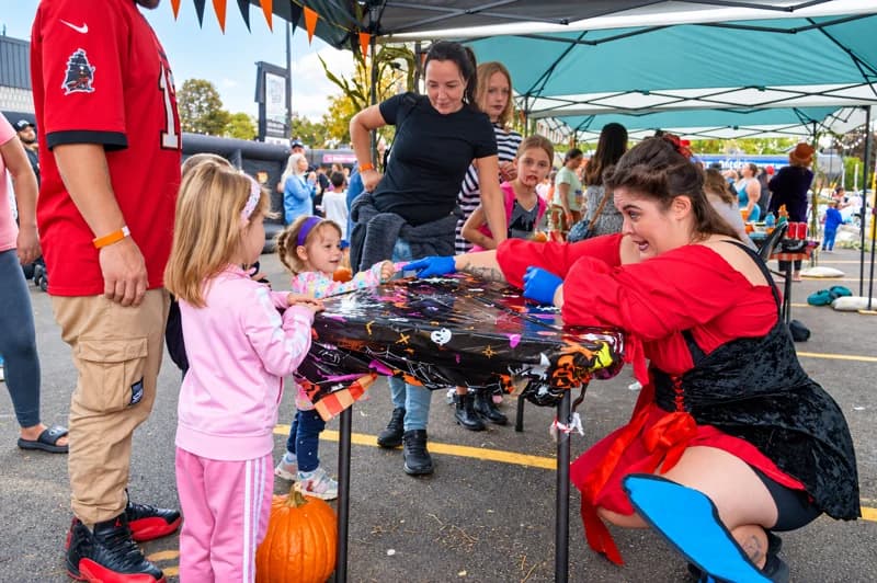 Children gather around a Halloween activity table with a costumed host.