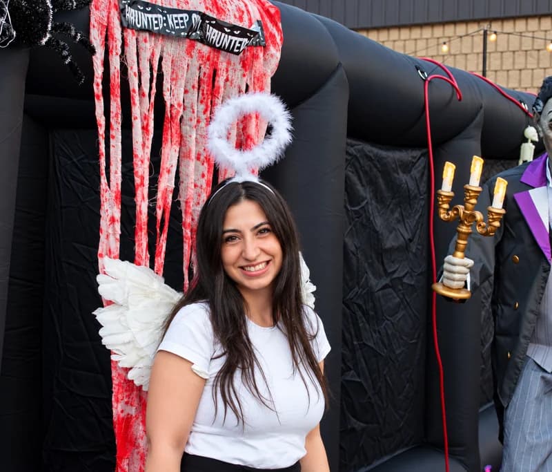 A smiling guest in a white top and halo poses beside the inflatable haunted-house entrance.
